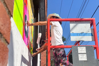 Artist on a lift painting the Take the Risk to Cool down mural