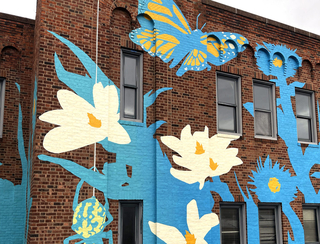 Blue and white abstract cooling mural on a brick building. White flowers, butterfly and spider are in scene.