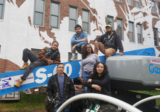 A group of 6 painters and apprentices climbing over a safety lift in front of the Mural